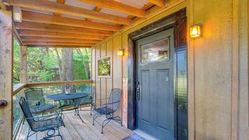 Une terrasse en bois avec une porte noire, deux chaises en métal et une table.
