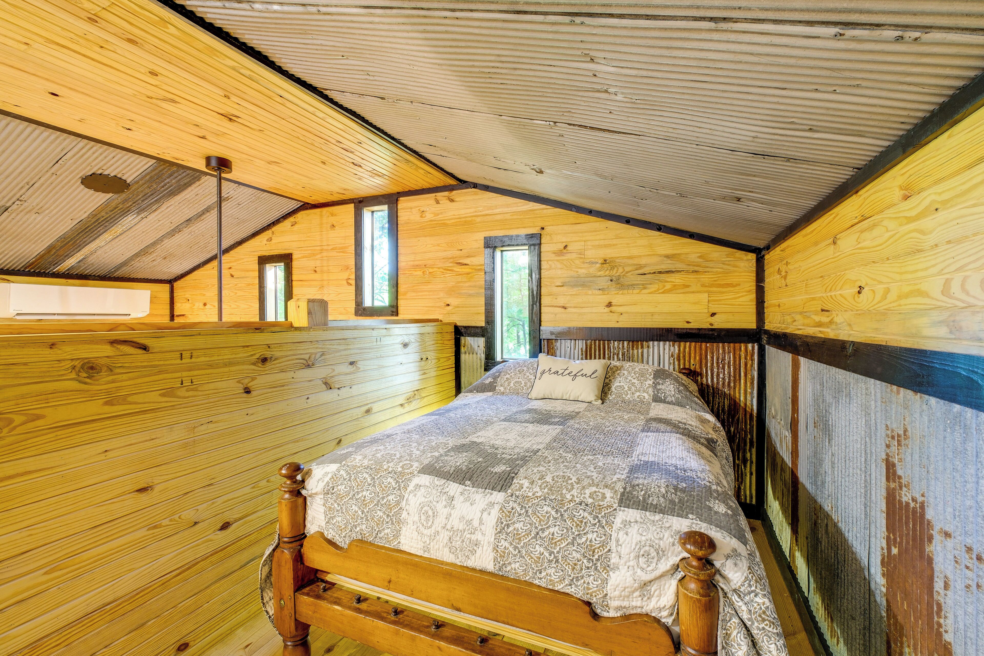 A wooden interior with a bed, a window, and a sloped ceiling.