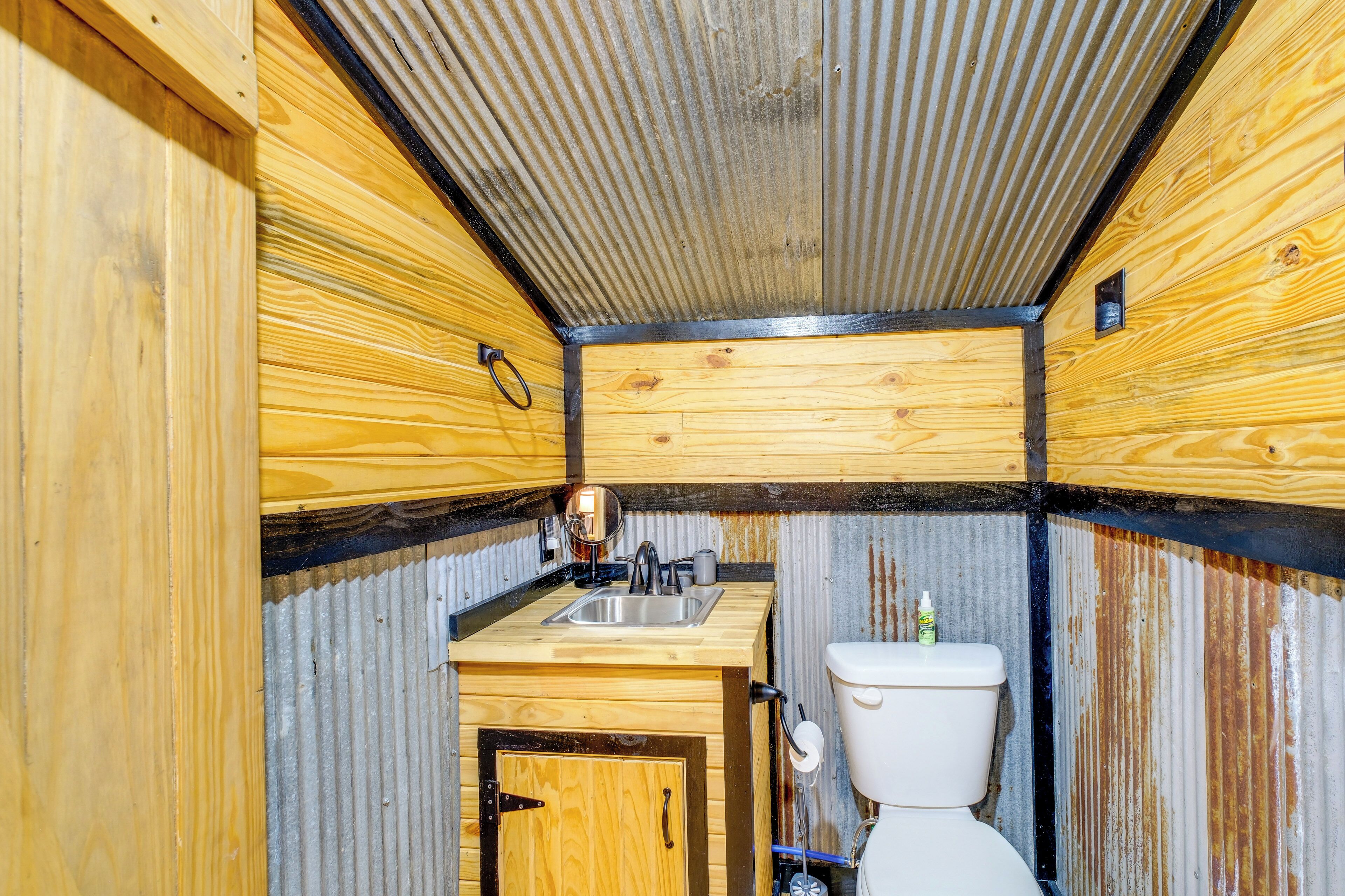 Una cabaña de madera compacta con kitchenette, un inodoro y techo de metal.