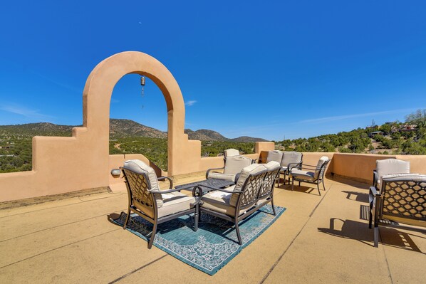 A rooftop terrace with outdoor furniture, a large arch structure, and a view of distant hills.