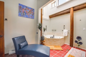 A bathroom with a bathtub, a wooden bench, a chair, and a painting on the wall.