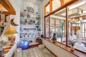 Ein gemütliches Zimmer mit großem Fenster, Holzbalken, Regalen mit Dekoration, einem blauen Gymnastikball und einem Schild mit der Aufschrift 'THIS FAMILY IS'.
