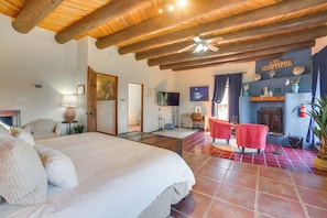 A spacious bedroom with a large bed, a television, a fireplace, and a ceiling fan.