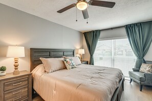 Ein Schlafzimmer mit einem Bett, Nachttischen, einem Deckenventilator und einem Fenster mit Vorhängen.
