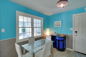 Une piĂšce avec une table en verre, des chaises blanches, un meuble bleu et une porte blanche.