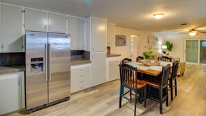 Une cuisine moderne équipée d’appareils électroménagers en acier inoxydable, un coin repas avec des tables et des chaises en bois, et un salon avec un canapé et une plante.