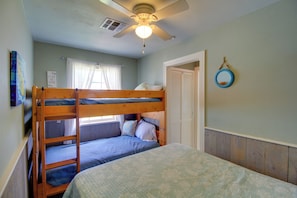 Une chambre avec un lit superposĂ©, un ventilateur de plafond, une fenĂȘtre avec des rideaux et une porte.