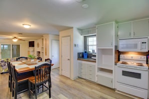 Une cuisine avec des meubles blancs, un four Ă micro-ondes, un four traditionnel, une table Ă manger avec des chaises et un ventilateur de plafond.