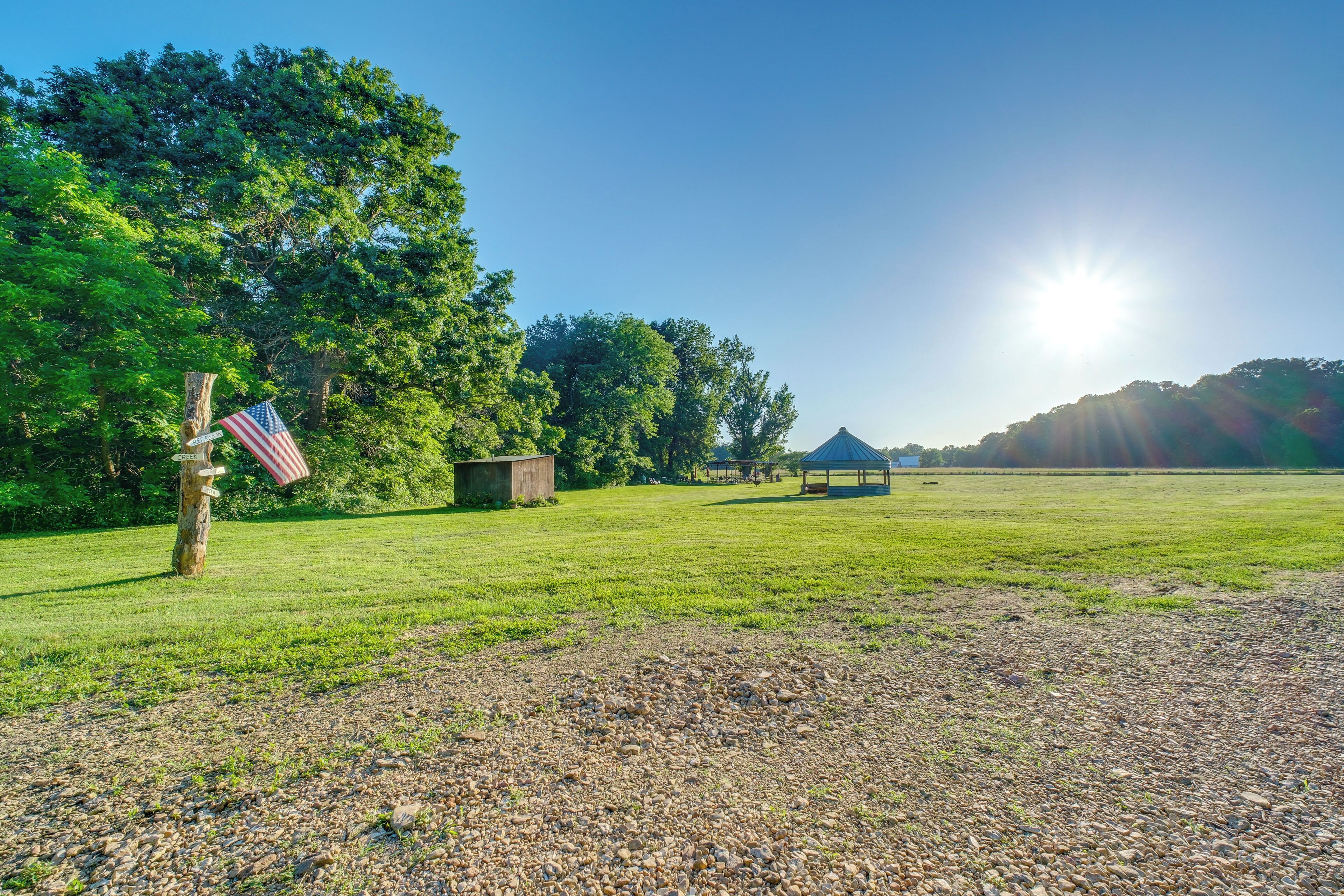 A grassy field with a flag, a small shed, and a gazebo under a clear sky.