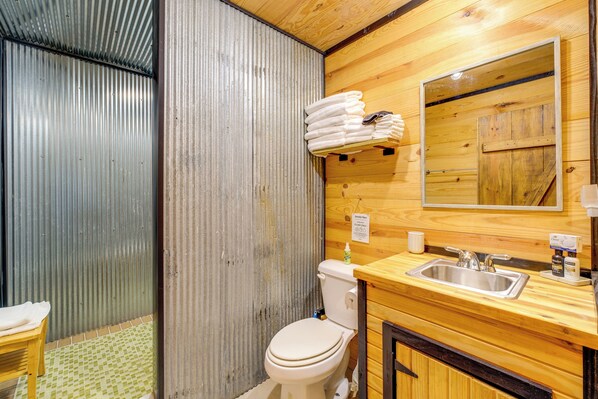 A bathroom with a toilet, sink, mirror, and wooden walls.