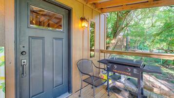 Eine Holzterrasse mit Grill, einer Tür mit Fenster und einem Stuhl.