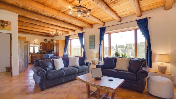 Ein geräumiges Wohnzimmer mit zwei Sofas, einem Couchtisch und einem Laptop. Das Zimmer verfügt über Holzbalkendecken und große Fenster mit Vorhängen.