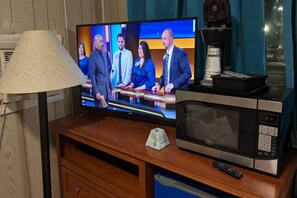 Uma televisão exibindo um programa de notícias, um micro-ondas, um controle remoto e uma lixeira.