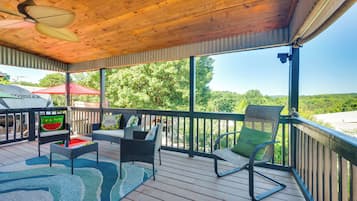 Une terrasse extérieure couverte, aménagée avec des meubles en osier, un ventilateur de plafond et offrant une vue sur la verdure environnante.