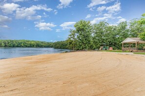 Una playa con una zona arenosa, una estructura de madera y un lago con árboles al fondo.