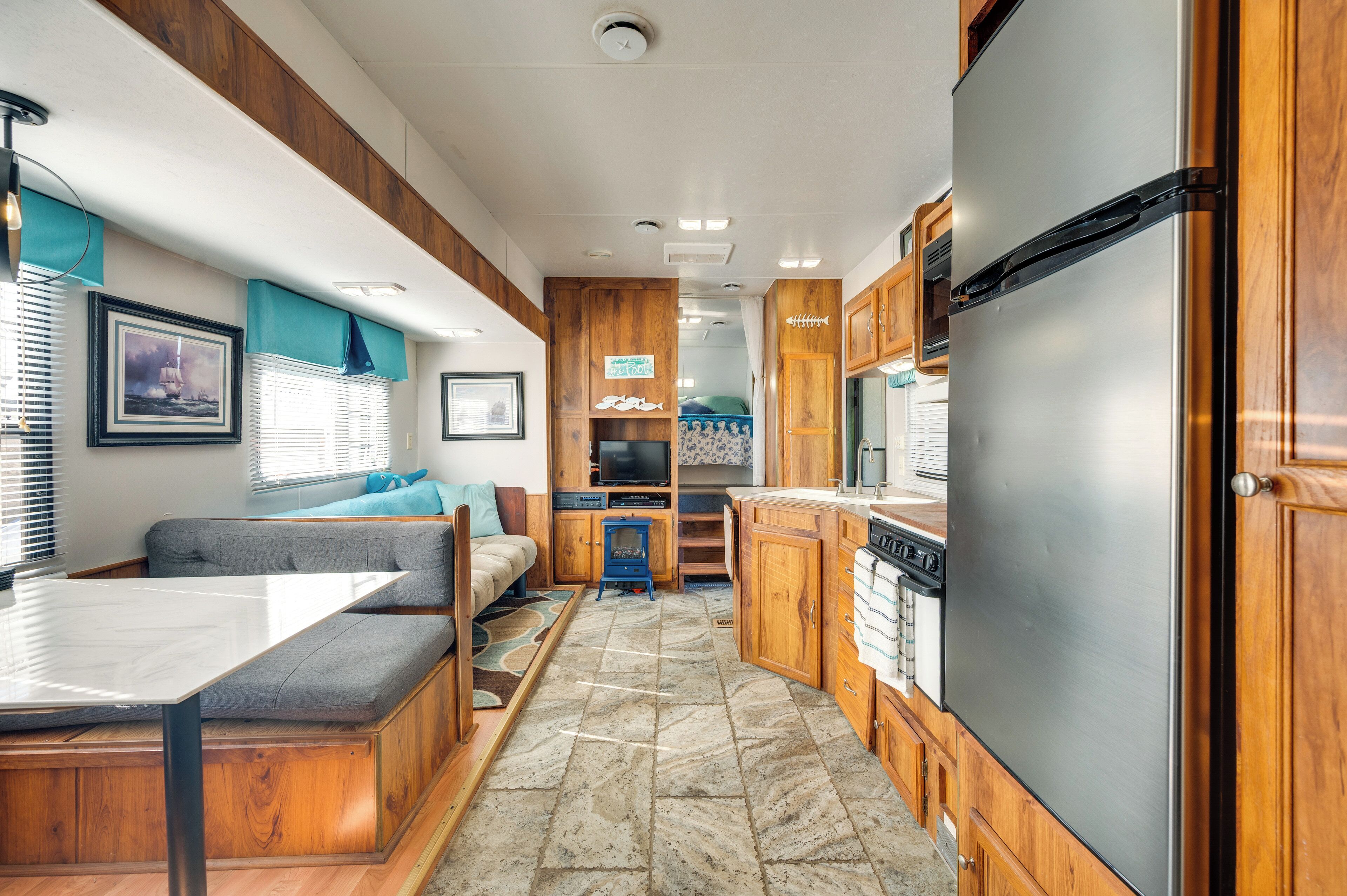 Une cuisine compacte pour camping-car, dotée de meubles en bois, d’un réfrigérateur en acier inoxydable, d’un coin repas avec une banquette et d’un petit téléviseur.