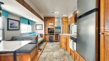 Une cuisine compacte pour camping-car, dotée de meubles en bois, d’un réfrigérateur en acier inoxydable, d’un coin repas avec une banquette et d’un petit téléviseur.