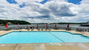 Ein Schwimmbad mit Liegestühlen und Sonnenschirmen, Blick auf das Wasser und ein bewölkter Himmel.