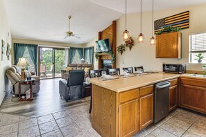 Een ruime keuken met een groot eiland, houten kastjes, een flatscreen televisie en een eethoek met stoelen en een tafel.
