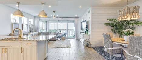 A spacious kitchen with a large island, dining area with wicker chairs, and a view to the outside.