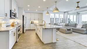 Una cocina moderna con armarios blancos, una isla central y una zona de comedor con sofá y alfombra.