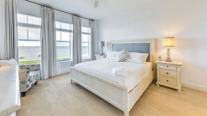 Un dormitorio con cama, mesita de noche, lámpara, silla y vista al exterior.