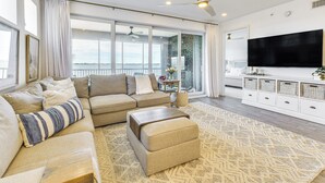 Un salón amplio con un sofá grande, un reposapiés y un televisor de pantalla plana montado en la pared.
