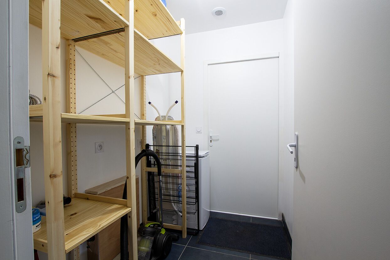 A compact room with built-in wooden shelving, a vacuum cleaner, and a white door.