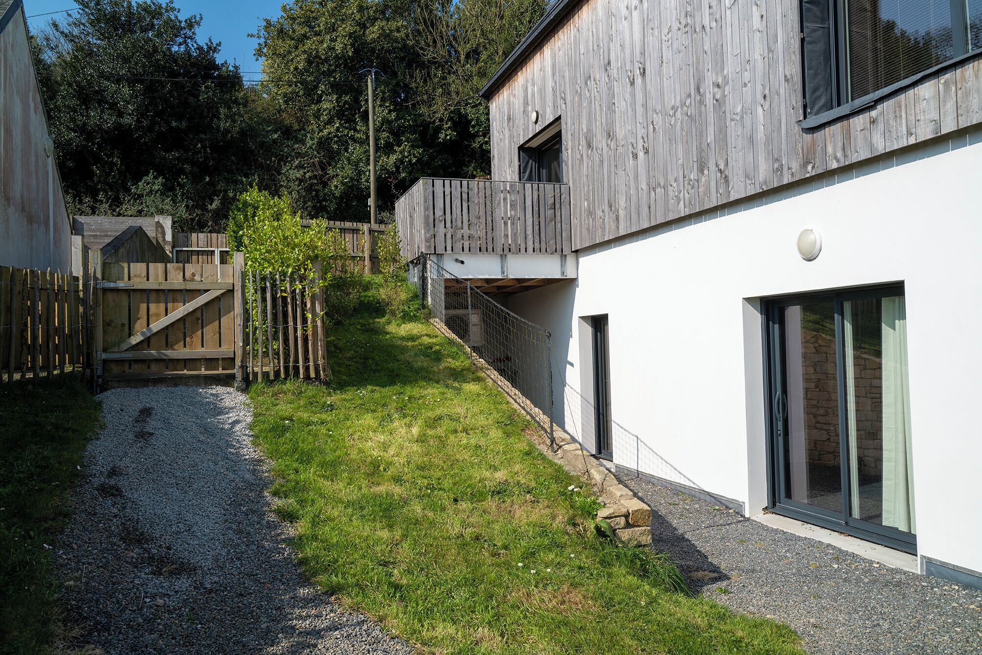 Un bâtiment moderne avec une façade en bois, un chemin de gravier et une clôture en bois.