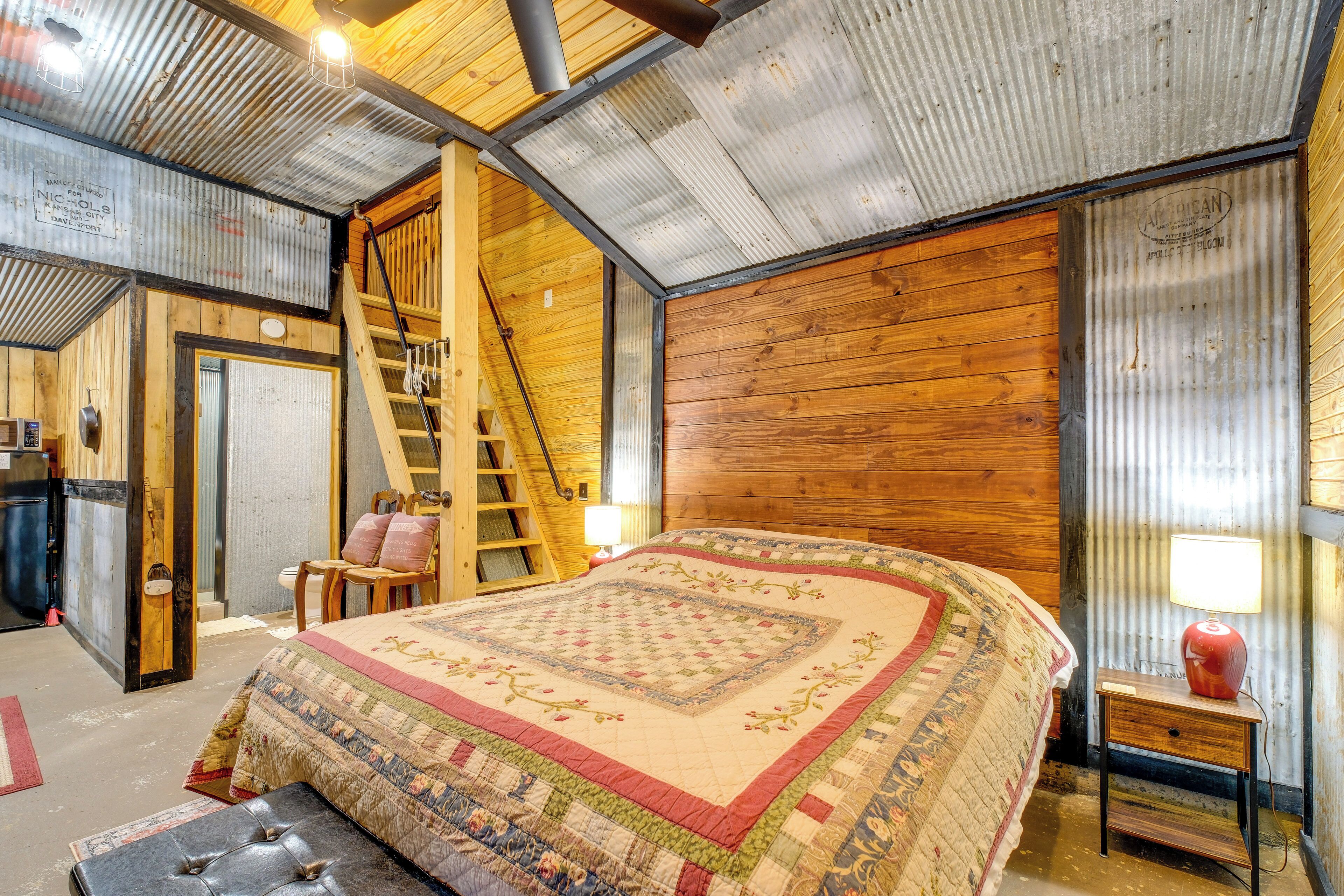 Une pièce rustique avec un grand lit, des murs en bois, une échelle, un bureau et une chaise.