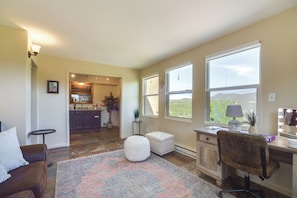 A spacious living area with a large window, a cozy seating area, and a kitchen in the background.