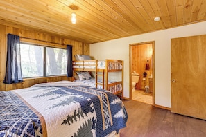 Ein Zimmer mit Holzwänden, einem Bett, einem Schlafstockbett und einer Tür zu einem Badezimmer.