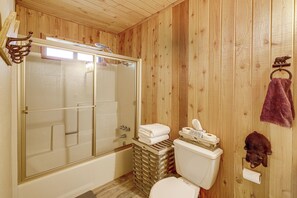 Een badkamer met houten lambrisering, een douchecabine van glas, een toilet en een beren decoratie.