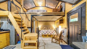 Interior acolhedor de uma cabana com quarto no mezanino, escada de madeira, área de jantar e cozinha.