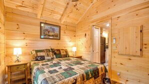 Ein Schlafzimmer einer Holzhütte mit einem Bett, Nachttischen, einem gerahmten Bild und einer Tür.