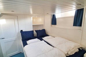 A compact room with two beds, a door, a small window with curtains, and a white ceiling.