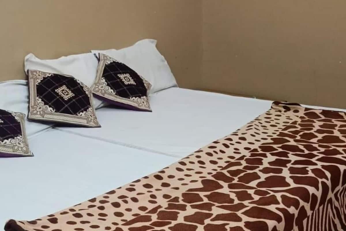 A bed with a white mattress, a brown and white patterned blanket, and decorative pillows.