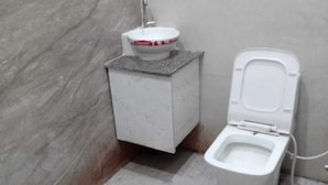 A bathroom with a toilet, a sink, and a marble wall. - Deva Guest House (Ayodhya)