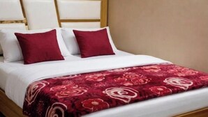 A bed with a white headboard, two red pillows, and a red floral bedspread. - Deva Guest House (Ayodhya)