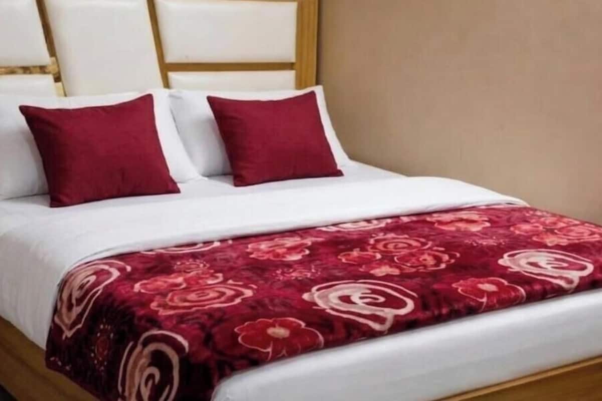 A bed with a white headboard, two red pillows, and a red floral bedspread.