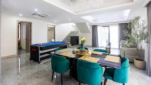 Ein modernes Wohnzimmer mit Billardtisch, einem Essbereich mit grünen Stühlen, einer Treppe und einem Kronleuchter.