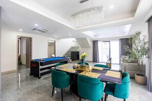 A modern living room with a pool table, a dining area with green chairs, a staircase, and a chandelier. - Facai Star Villa A22 (Banglamung)