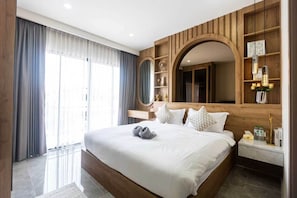 Een moderne hotelkamer met een groot bed, een houten hoofdbord, een inbouwkast met decoratieve objecten en een groot raam met gordijnen.
