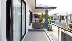 Ein modernes Wohngebäude mit einem Glasbalkon, einem Essbereich mit Gartenmöbeln und Blick auf benachbarte Häuser.