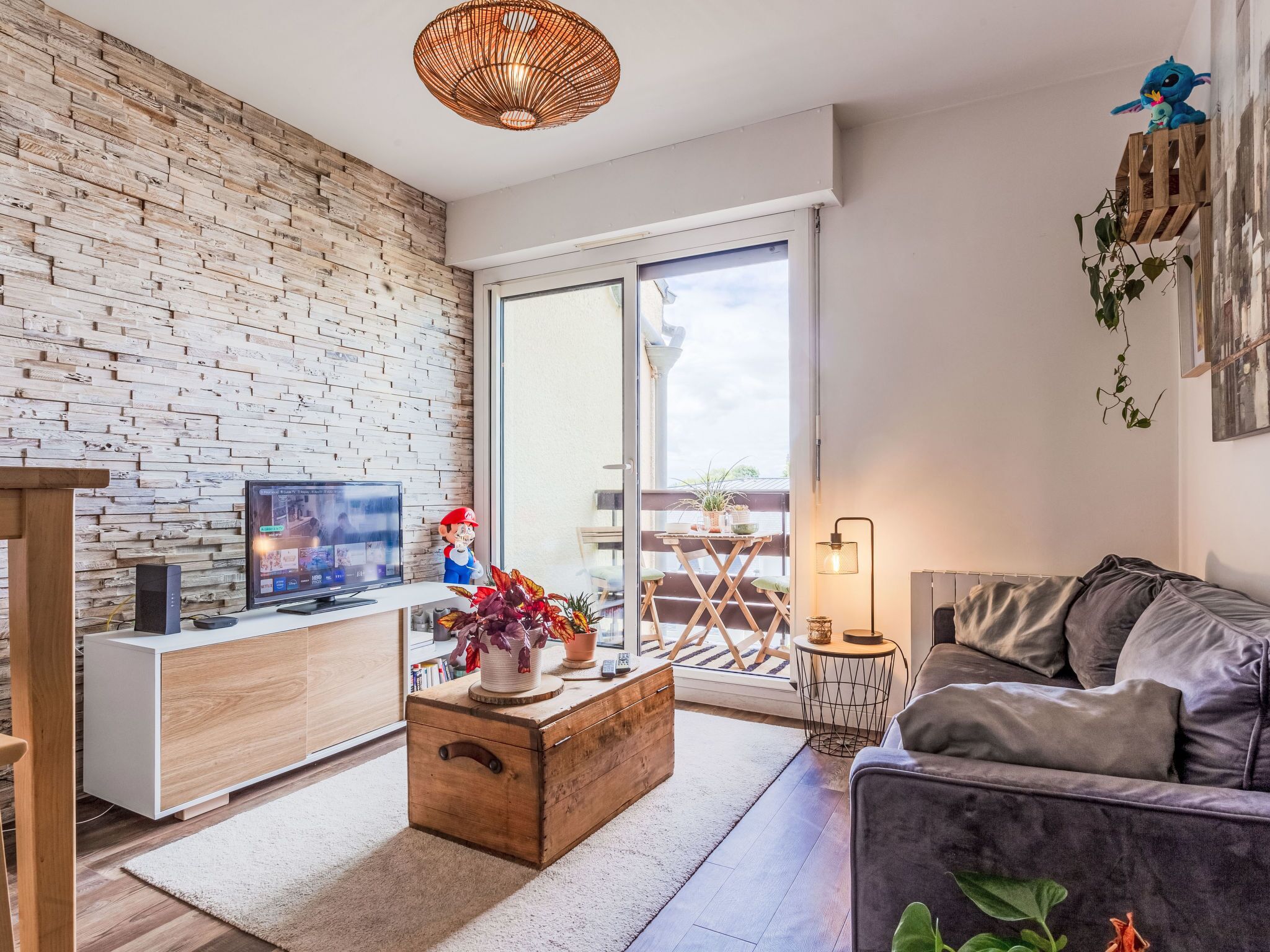 Un salon avec un mur en briques, une table basse en bois, un canapé gris, un téléviseur et une porte-fenêtre coulissante donnant sur un espace extérieur.