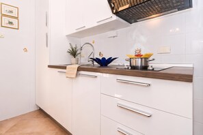 A modern kitchen with white cabinets, a wooden countertop, a stainless steel sink, and a range hood. - Marisa Olive Grove Apartments (Labin)