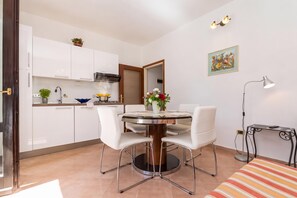 Une cuisine compacte avec des meubles blancs, une cuisinière et un coin repas comprenant une table ronde et des chaises blanches.