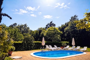 Une piscine entourée d’une végétation luxuriante, avec des chaises longues et des parasols.