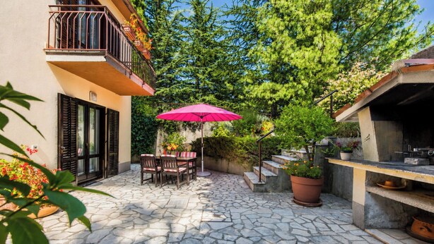 A stone-tiled patio with a table and chairs, a pink umbrella, and potted plants. - Marisa Olive Grove Apartments (Labin)