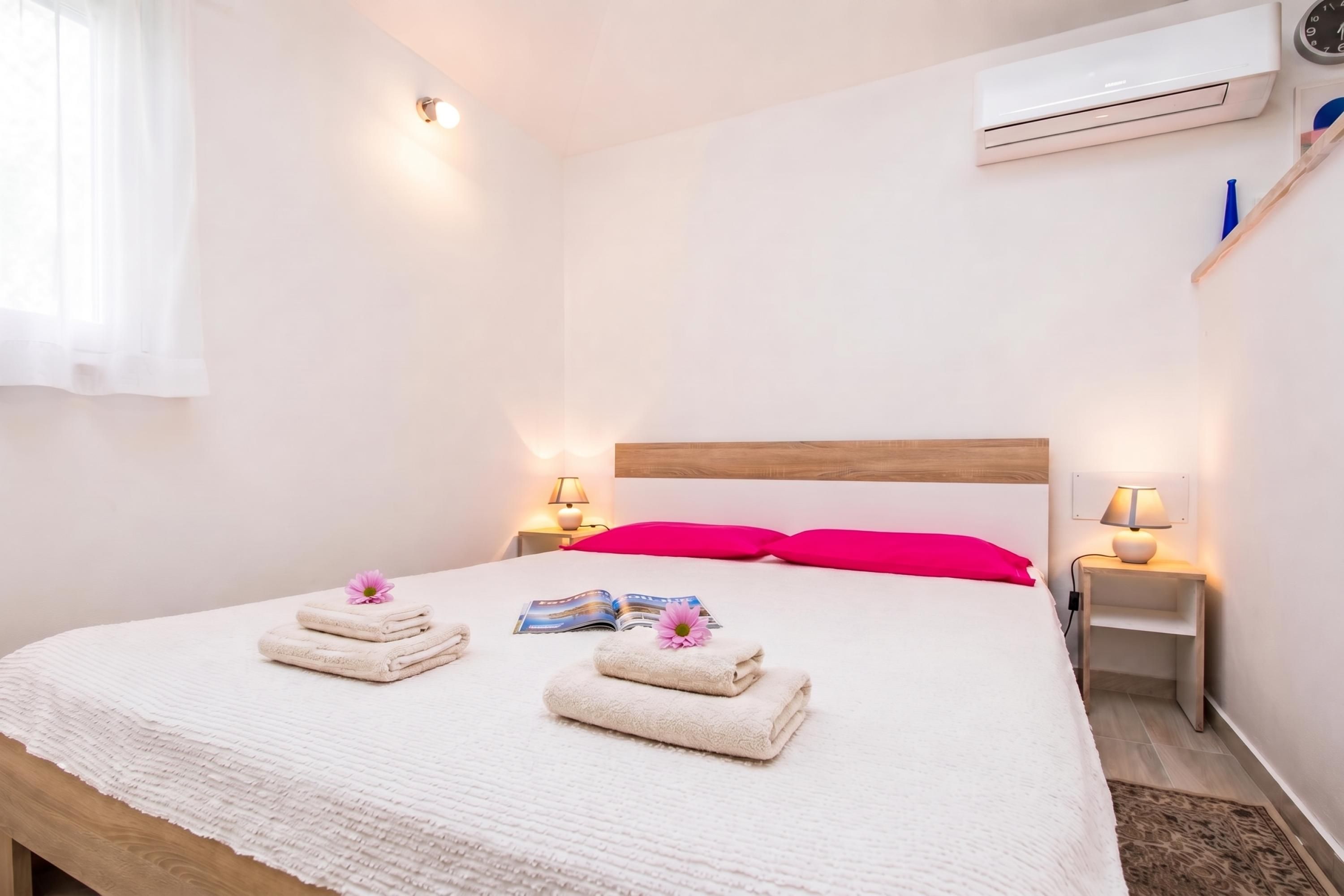 Una habitación de hotel con una cama, dos lámparas de noche, aire acondicionado y una ventana con cortinas.
